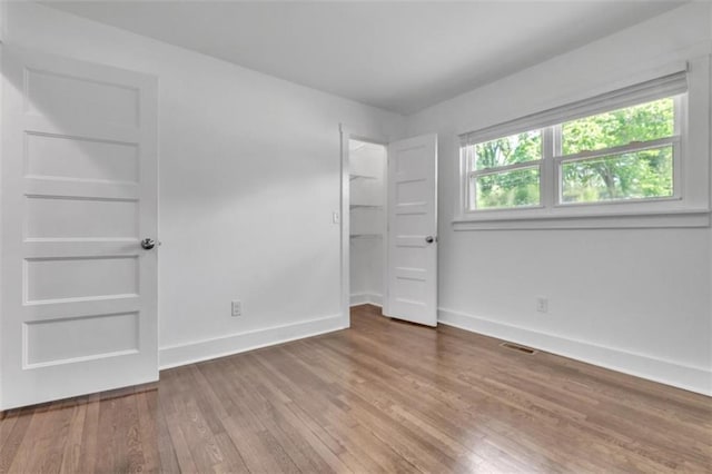 unfurnished bedroom featuring wood finished floors, baseboards, a closet, and visible vents