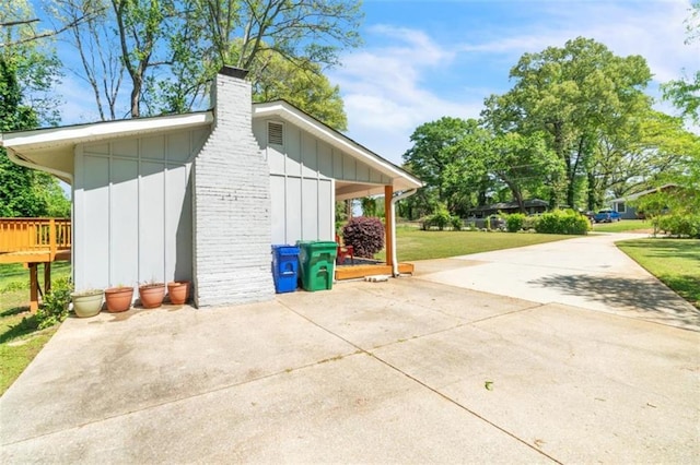 exterior space featuring a yard, driveway, board and batten siding, and a chimney