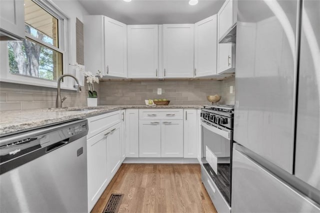 kitchen with white cabinets, a sink, appliances with stainless steel finishes, light wood finished floors, and light stone counters