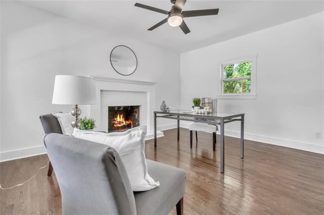 home office featuring a brick fireplace, baseboards, a ceiling fan, and wood finished floors