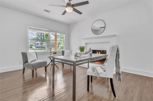 dining room with a ceiling fan, visible vents, wood finished floors, a brick fireplace, and baseboards
