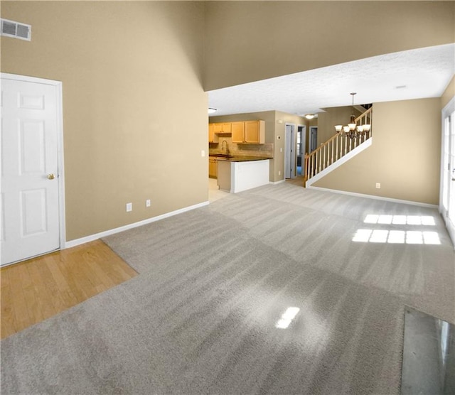 unfurnished living room featuring a textured ceiling, sink, a chandelier, and light colored carpet