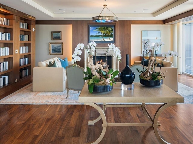 living area featuring a lit fireplace, a tray ceiling, and wood finished floors