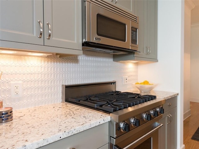 kitchen featuring appliances with stainless steel finishes, gray cabinets, light stone countertops, and decorative backsplash