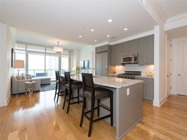 kitchen featuring stove, gray cabinets, decorative backsplash, stainless steel microwave, and crown molding