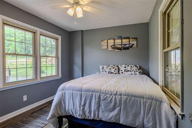 bedroom with ceiling fan, a textured ceiling, baseboards, and wood finished floors