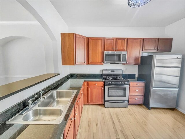 kitchen featuring dark countertops, light wood-style flooring, stainless steel appliances, and a sink