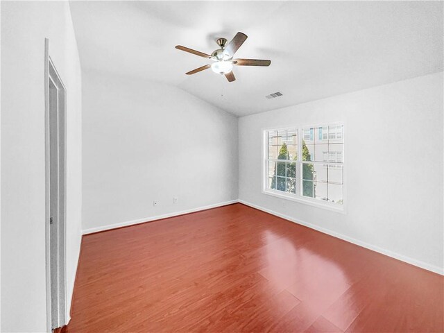 empty room with visible vents, wood finished floors, baseboards, ceiling fan, and vaulted ceiling