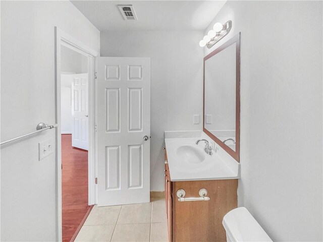 half bathroom with visible vents, toilet, vanity, and tile patterned flooring