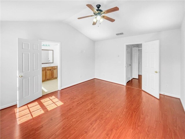 unfurnished bedroom featuring visible vents, baseboards, lofted ceiling, ensuite bathroom, and wood finished floors