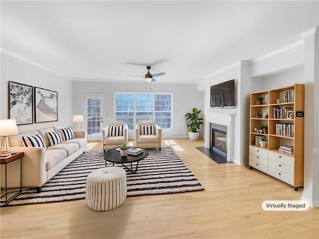 living room featuring a fireplace with flush hearth, a ceiling fan, wood finished floors, and crown molding