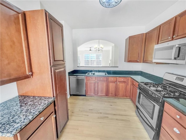 kitchen featuring brown cabinets, light wood-style flooring, a sink, stainless steel appliances, and arched walkways