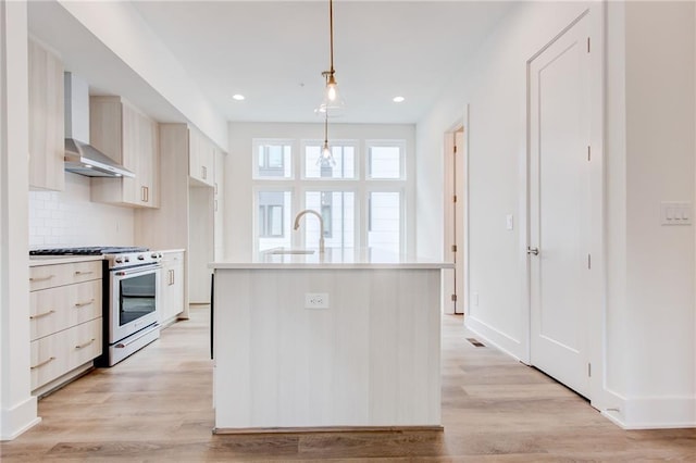 kitchen with decorative light fixtures, light wood-type flooring, stainless steel range with gas cooktop, an island with sink, and wall chimney range hood