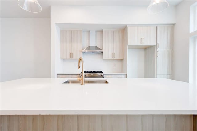 kitchen with hanging light fixtures, sink, wall chimney range hood, and light brown cabinetry