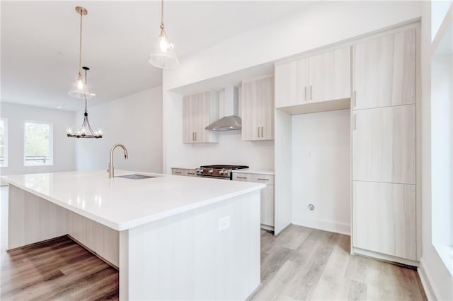 kitchen featuring sink, an island with sink, stainless steel stove, pendant lighting, and wall chimney range hood