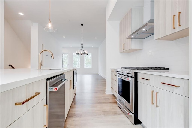 kitchen with sink, decorative light fixtures, light hardwood / wood-style flooring, appliances with stainless steel finishes, and wall chimney range hood