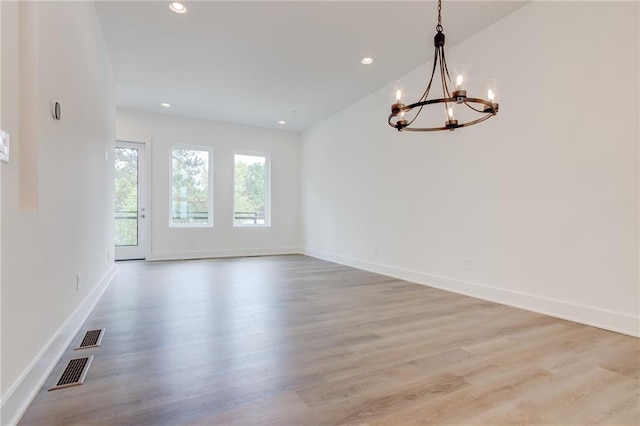 unfurnished room featuring an inviting chandelier and light wood-type flooring