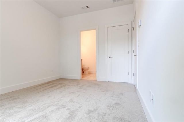 unfurnished bedroom featuring light carpet and connected bathroom