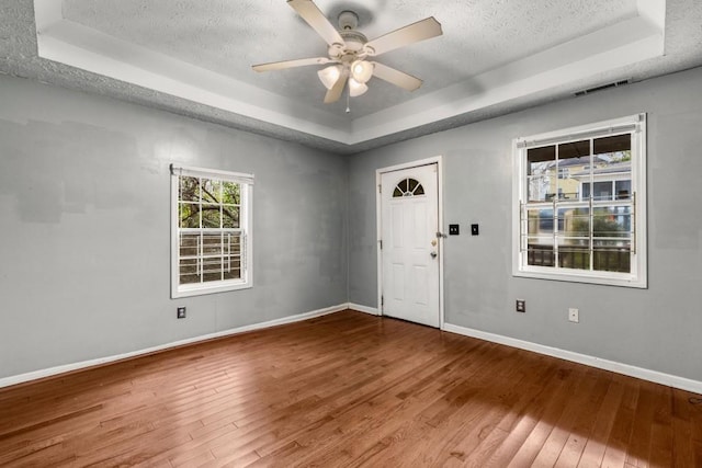 interior space with wood-type flooring, ceiling fan, a textured ceiling, and a tray ceiling