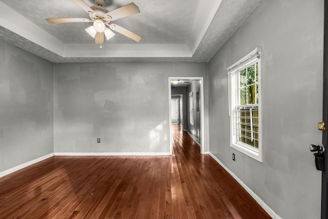 unfurnished room with dark hardwood / wood-style flooring, ceiling fan, a tray ceiling, and a textured ceiling