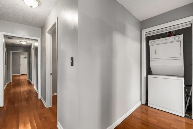 corridor with wood-type flooring, stacked washer and clothes dryer, and a textured ceiling