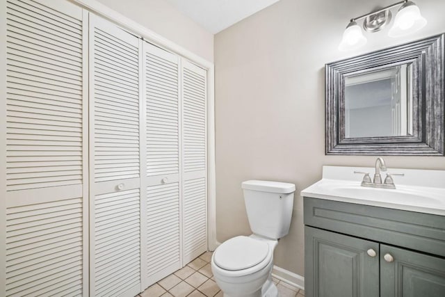 half bathroom with tile patterned flooring, toilet, vanity, baseboards, and a closet