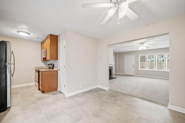 kitchen featuring light colored carpet, stainless steel appliances, a fireplace with flush hearth, visible vents, and brown cabinetry