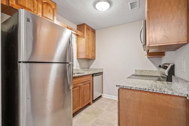 kitchen featuring light stone counters, stainless steel appliances, visible vents, a textured ceiling, and baseboards