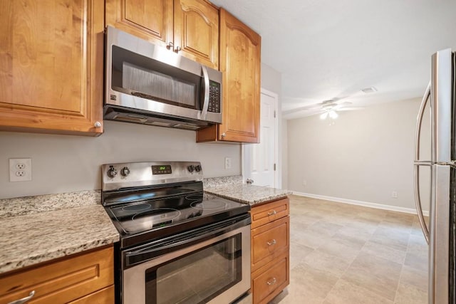 kitchen with baseboards, brown cabinetry, a ceiling fan, light stone countertops, and stainless steel appliances