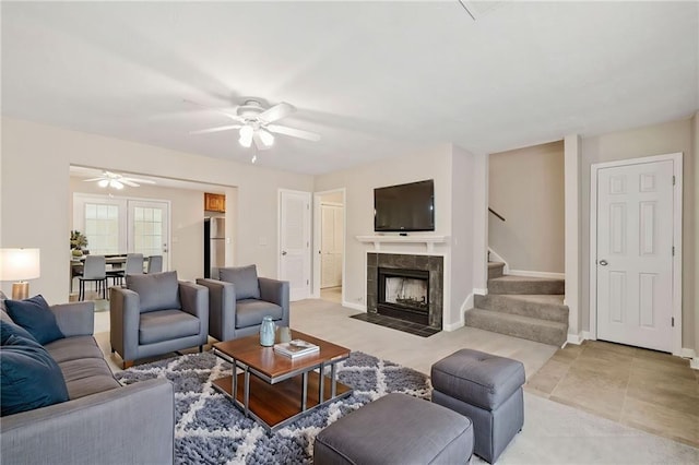 living area with stairs, ceiling fan, a tiled fireplace, and baseboards