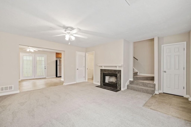 unfurnished living room with carpet floors, visible vents, a tiled fireplace, ceiling fan, and stairs