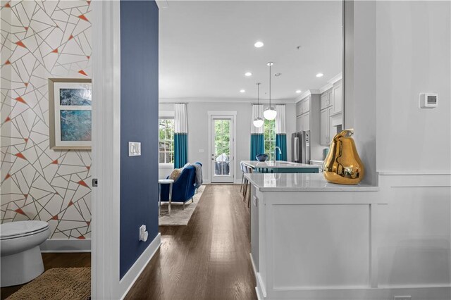 hall featuring crown molding, dark wood finished floors, recessed lighting, an accent wall, and baseboards