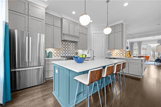 kitchen with a kitchen island with sink, a kitchen breakfast bar, light countertops, freestanding refrigerator, and decorative light fixtures