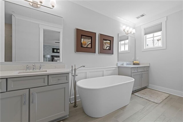 full bathroom with crown molding, two vanities, visible vents, a sink, and a freestanding tub