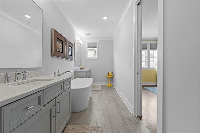 bathroom featuring wood finished floors, vanity, baseboards, a freestanding bath, and crown molding