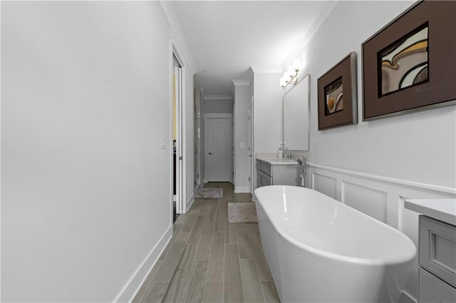 full bath with a decorative wall, wood finish floors, vanity, a soaking tub, and crown molding