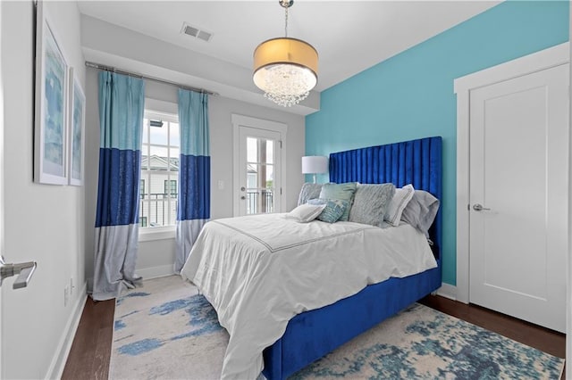 bedroom with an inviting chandelier, wood finished floors, visible vents, and baseboards