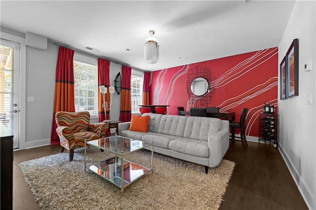 living room featuring an accent wall, dark wood-style flooring, visible vents, and baseboards