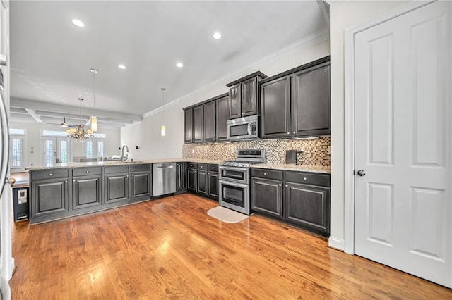 kitchen with a peninsula, light wood finished floors, ornamental molding, and stainless steel appliances