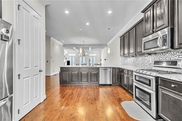 kitchen featuring stainless steel appliances, a peninsula, a sink, an inviting chandelier, and ornamental molding
