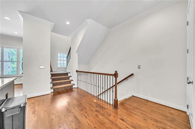 staircase featuring ornamental molding, baseboards, a healthy amount of sunlight, and wood finished floors