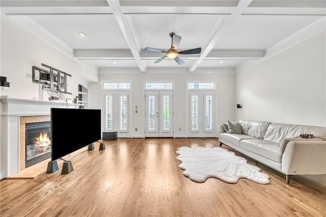 living room with a tile fireplace, a ceiling fan, wood finished floors, and beam ceiling