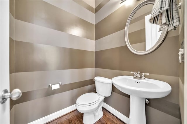 half bath featuring wood finished floors, toilet, and baseboards