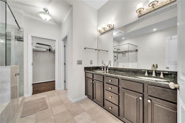 full bath with double vanity, a shower stall, a spacious closet, and a sink