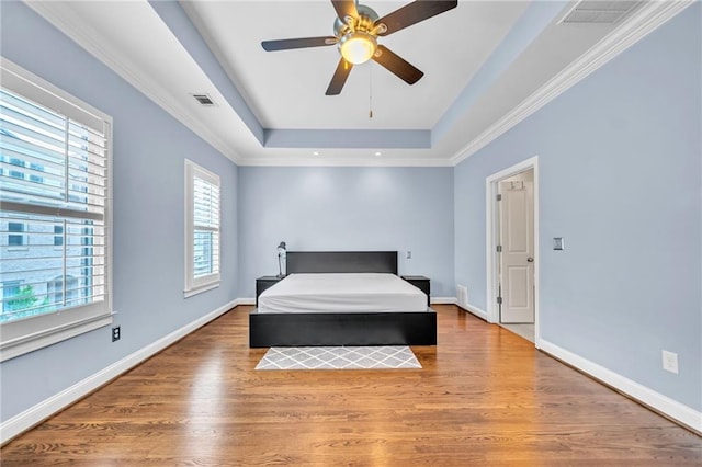 bedroom with a tray ceiling, baseboards, visible vents, wood finished floors, and ceiling fan