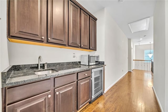 kitchen with dark stone counters, a sink, beverage cooler, light wood-style flooring, and stainless steel microwave