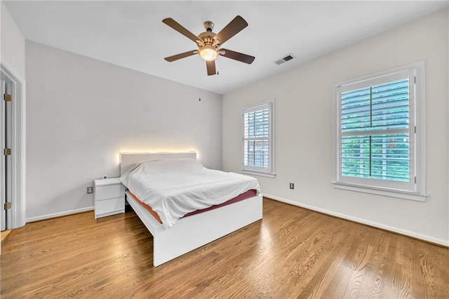 bedroom featuring baseboards, wood finished floors, visible vents, and a ceiling fan