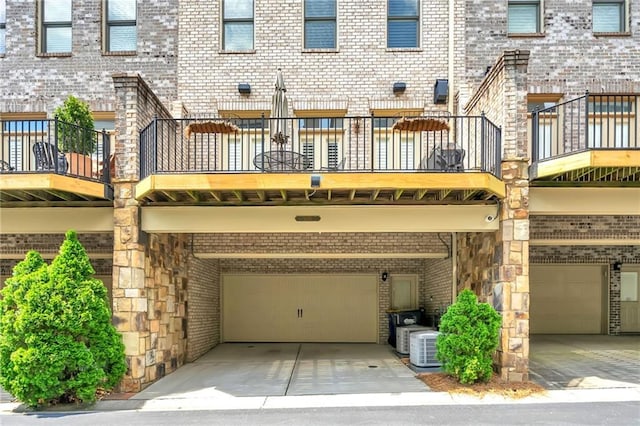 rear view of property with a balcony, brick siding, and a garage