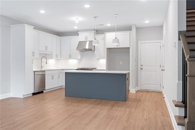 kitchen with stainless steel dishwasher, light hardwood / wood-style flooring, pendant lighting, wall chimney exhaust hood, and white cabinets