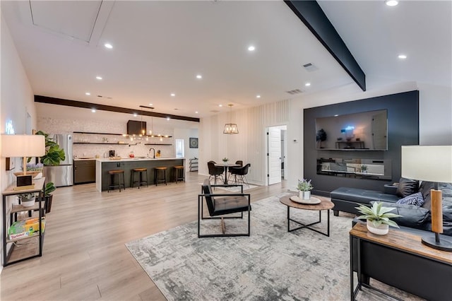 living room featuring light hardwood / wood-style flooring, a notable chandelier, beamed ceiling, and sink